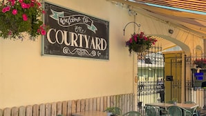 An outdoor seating area with a sign reading 'Welcome to the COURTYARD,' green metal chairs, and hanging flower baskets. - Arbutus Hotel Killarney (Killarney)