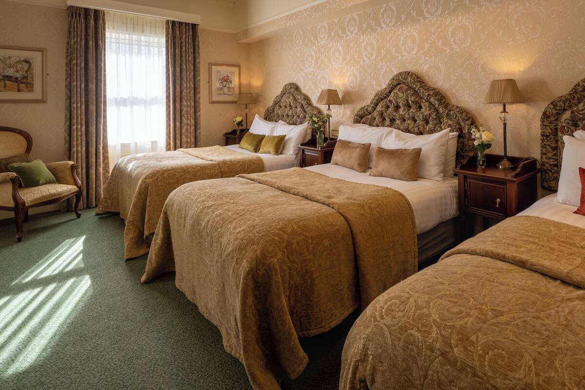 A hotel room with three beds, a chair, and a nightstand with lamps.