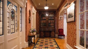 A hallway with wooden flooring, a patterned rug, a bookshelf, a red chair, and a framed picture on the wall. - Arbutus Hotel Killarney (Killarney)
