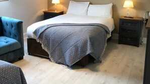 A bedroom with a bed, two bedside tables, a lamp, a blue armchair, and a painting on the wall. - Amber Hill Guesthouse (Galway)