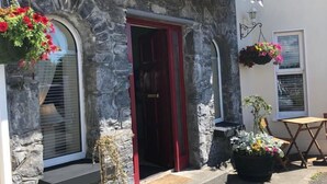 A stone building with a red door, two large flower pots, and a small patio area. - Amber Hill Guesthouse (Galway)
