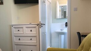 A room with a yellow sofa, a white dresser with drawers, a flat-screen TV mounted on the wall, and a bathroom visible through an open door. - Amber Hill Guesthouse (Galway)