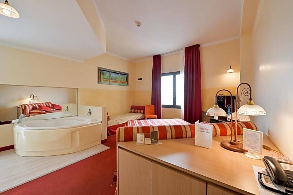 Una habitación de hotel con cama, escritorio, teléfono, lámpara y bañera.