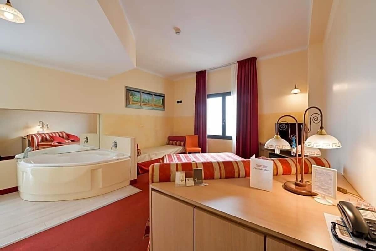 A hotel room with a bed, a desk, a telephone, a lamp, and a bathtub.