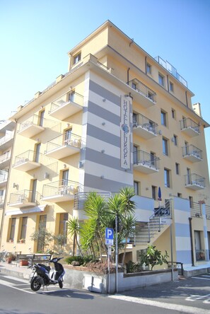 A multi-story hotel with balconies, a parking sign, and a scooter parked in front. - Hotel Europa (San Bartolomeo al Mare)