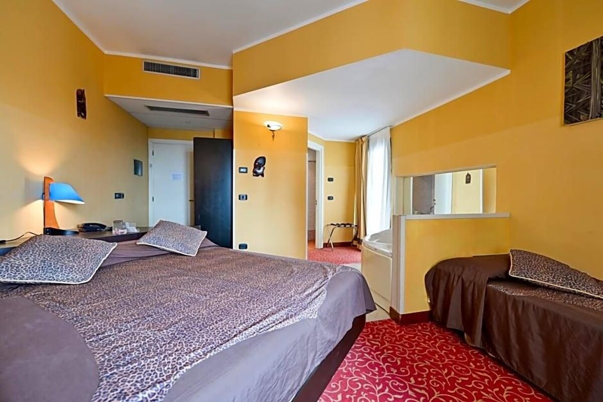 A hotel room with two beds, a desk, a chair, a mirror, and a red carpet.