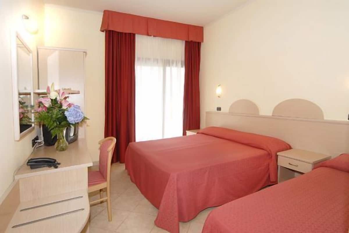 Habitación de hotel con dos camas, un escritorio con silla, un espejo y una ventana con cortinas.