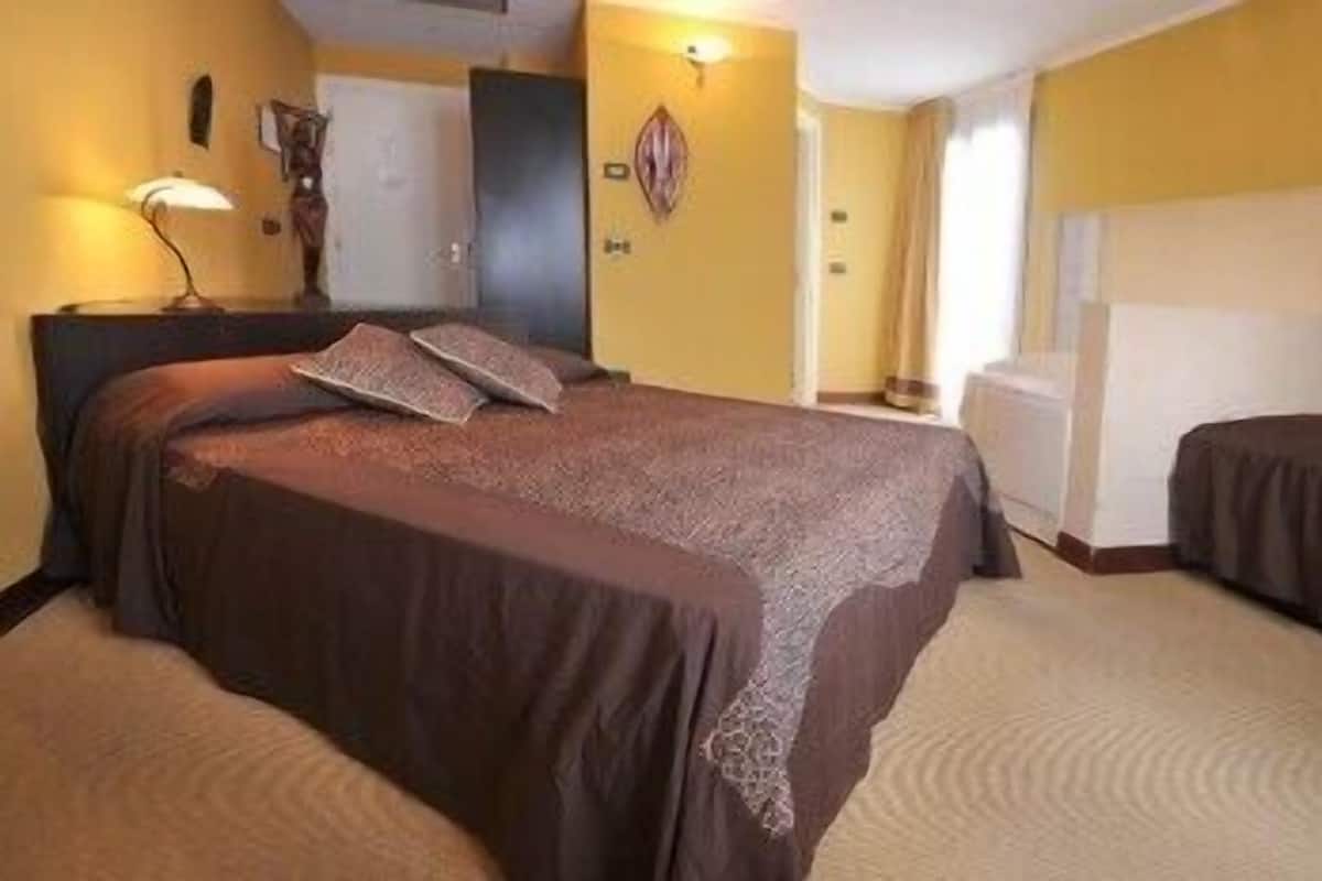 Una habitación de hotel con una cama grande, una mesita de noche, una lámpara y un armario.