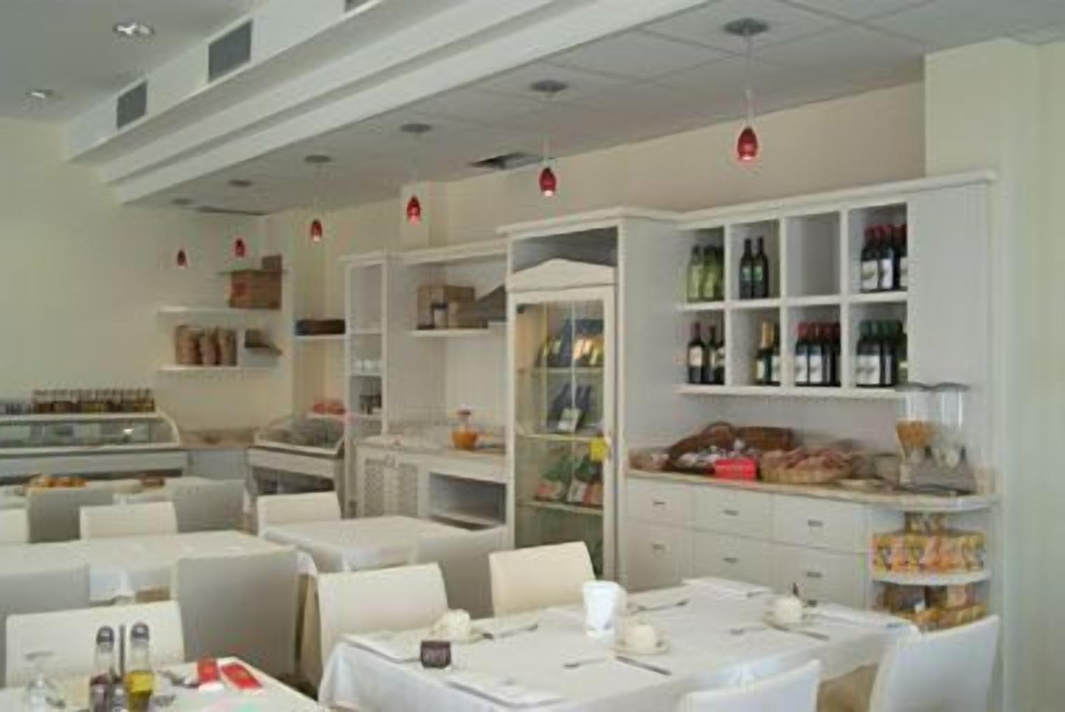 Un restaurante con mesas y sillas blancas, estantes con botellas y una barra con productos alimenticios.