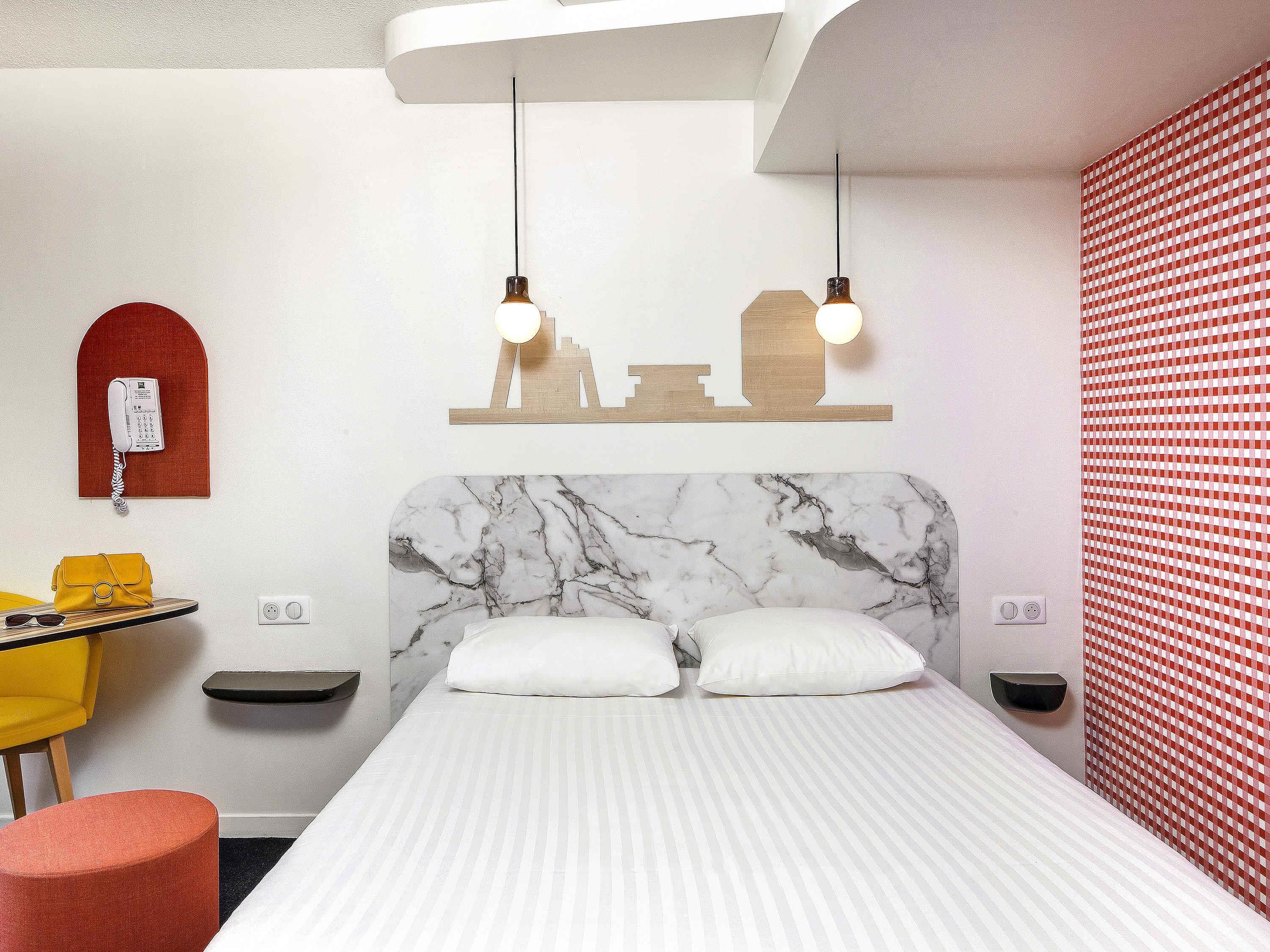 Habitación de hotel con una cama, un escritorio, una silla, un teléfono y una pared con estampado rojo.