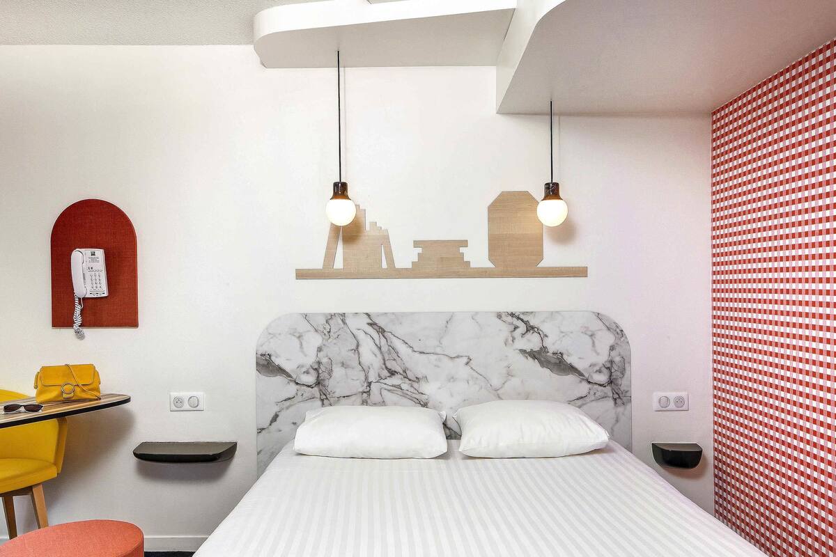 Ein Hotelzimmer mit Bett, Schreibtisch, Stuhl, Telefon und einer Wand mit rotem Muster.