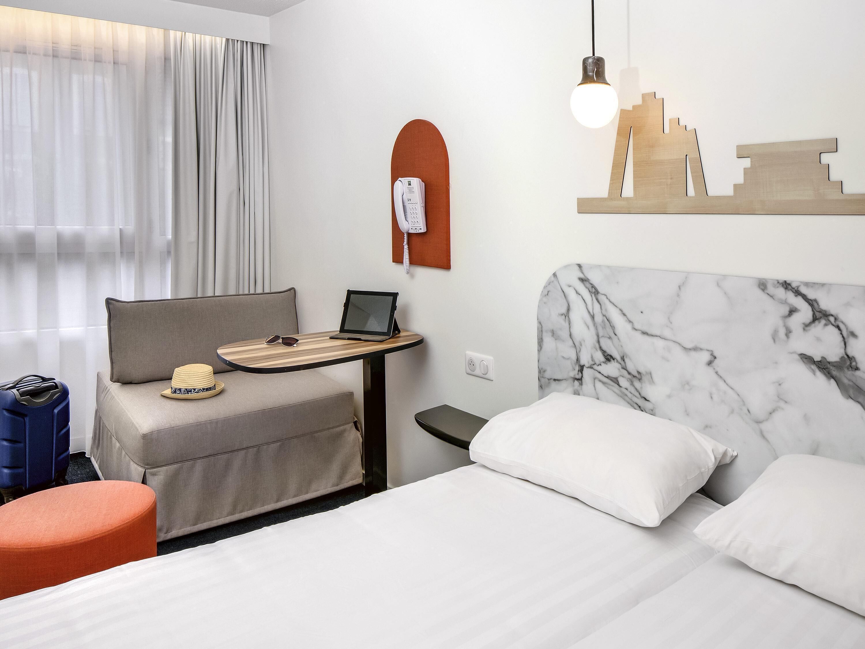 Habitación de hotel con una cama, un escritorio con una computadora portátil, un teléfono y una obra de arte urbana en la pared.