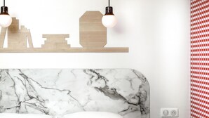 A bedroom with a marble headboard, two white pillows, a wooden shelf with cut-out shapes, and a red and white checkered wall. - ibis Styles Vichy Centre (Vichy)