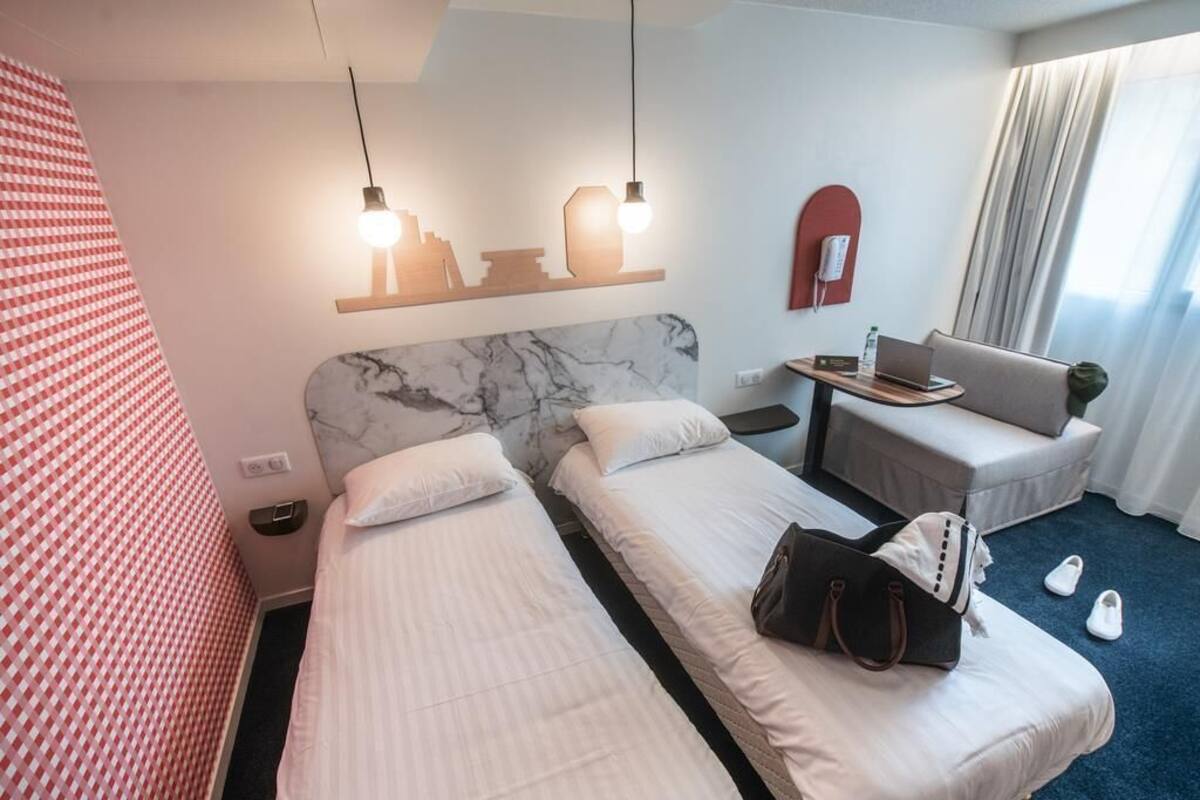Ein Hotelzimmer mit zwei Betten, einem Schreibtisch, einem Stuhl, einem Telefon und einem Fenster mit Vorhängen.