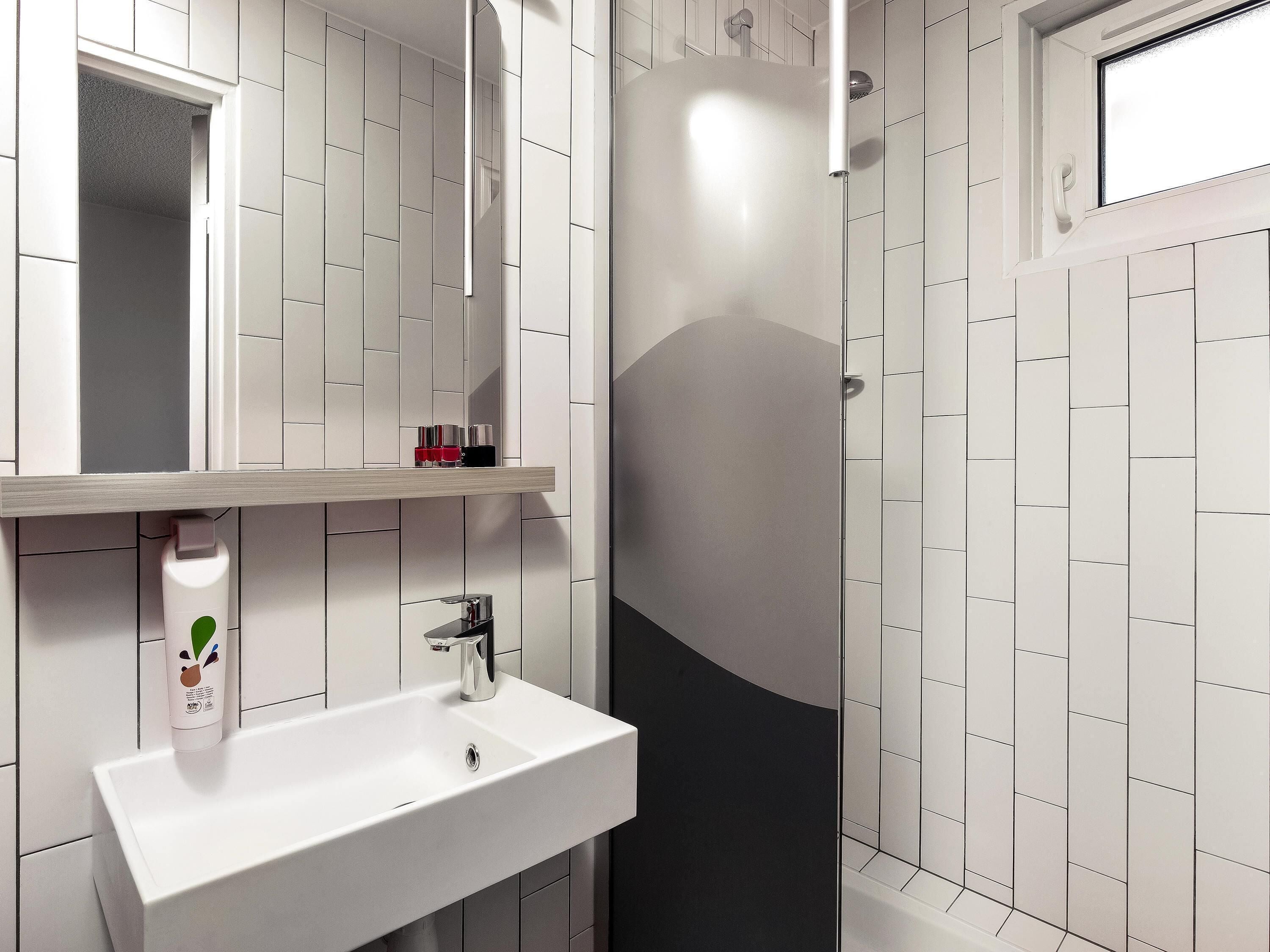 Un baño con lavamanos blanco, espejo y zona de ducha.