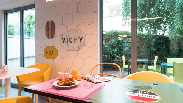 A dining area with a table set for two, a menu, and a glass of orange juice. - ibis Styles Vichy Centre (Vichy)