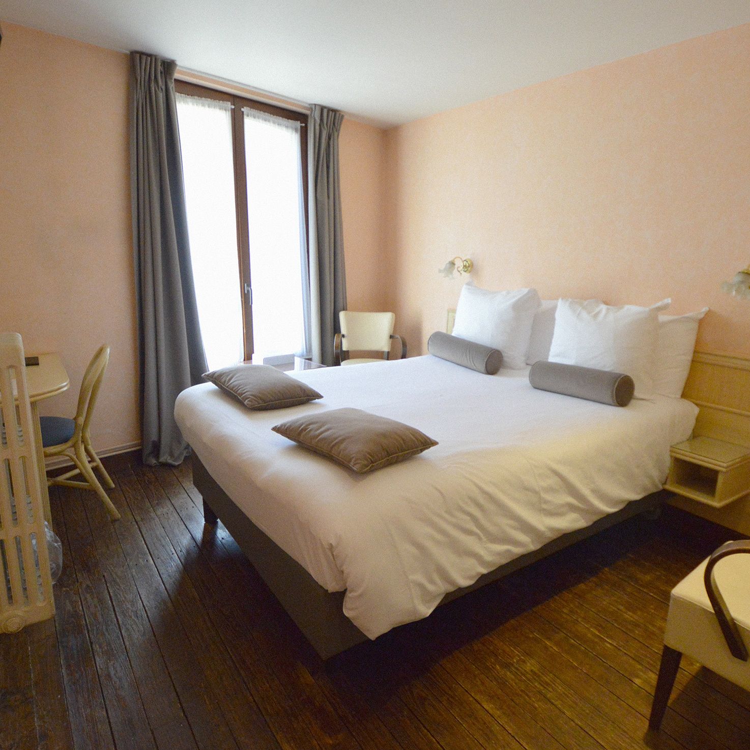 Habitación de hotel con una cama grande, una mesita de noche, una silla y una ventana con cortinas.