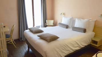 A hotel room with a large bed, a bedside table, a chair, and a window with curtains.
