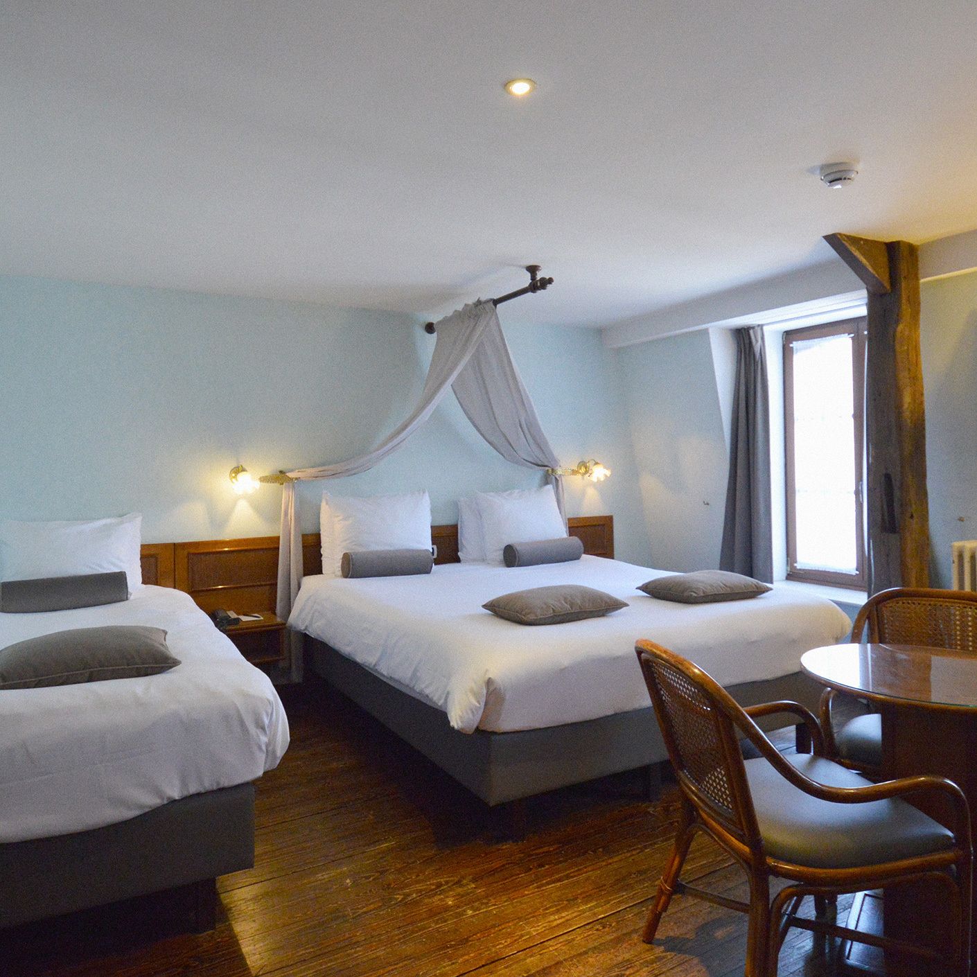 Une chambre d’hôtel avec deux lits, un plancher en bois, une table à manger avec des chaises et une fenêtre avec des rideaux.