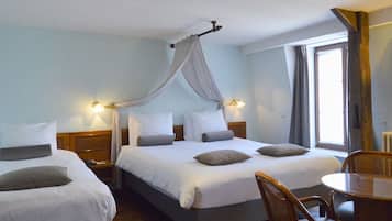 Une chambre d’hôtel avec deux lits, un plancher en bois, une table à manger avec des chaises et une fenêtre avec des rideaux.