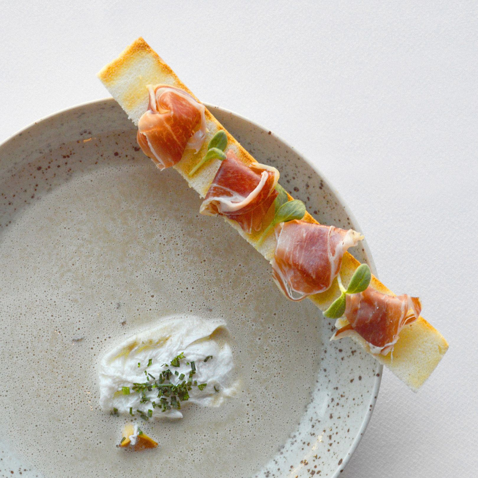 A dish with prosciutto and a creamy sauce on a plate.