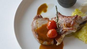 Une assiette avec une côtelette d’agneau, des tomates cerises et une petite coupelle de sauce.