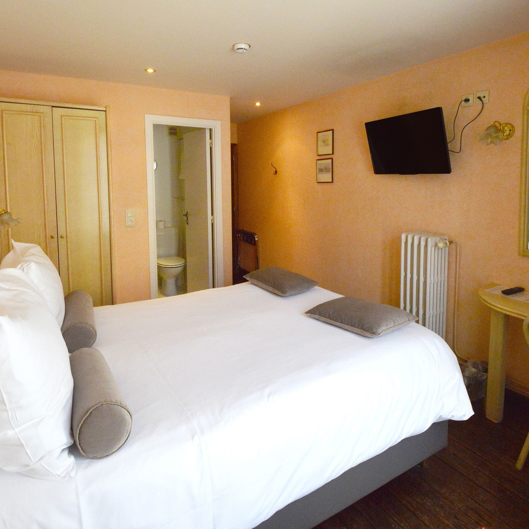Une chambre à coucher avec un lit, une table de chevet, un téléviseur et une salle de bain visible à travers une porte ouverte.
