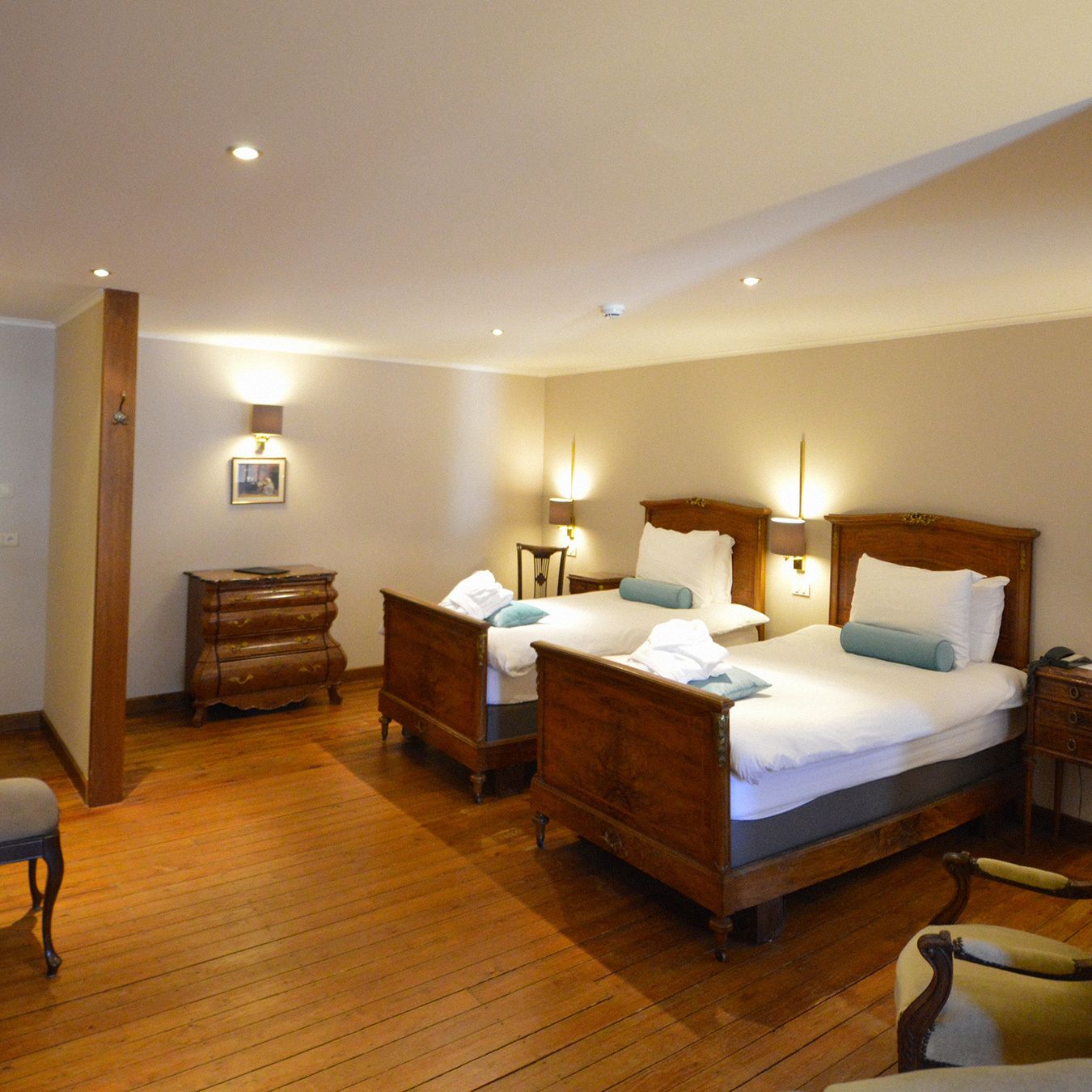 A hotel room with two wooden beds, a wooden dresser, a chair, and a desk with a lamp.