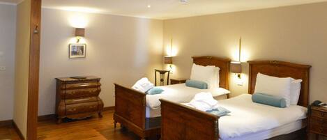 A hotel room with two wooden beds, a wooden dresser, a chair, and a desk with a lamp.