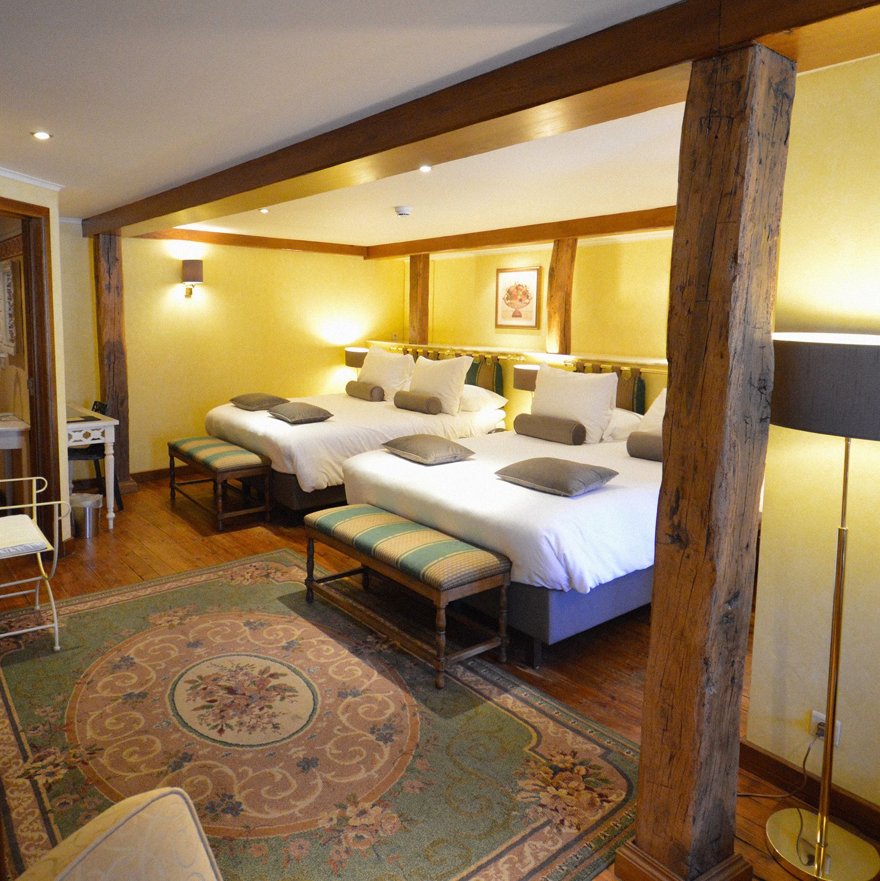 A hotel room with a large bed, two bedside tables, a bench, a small desk, and a chair.