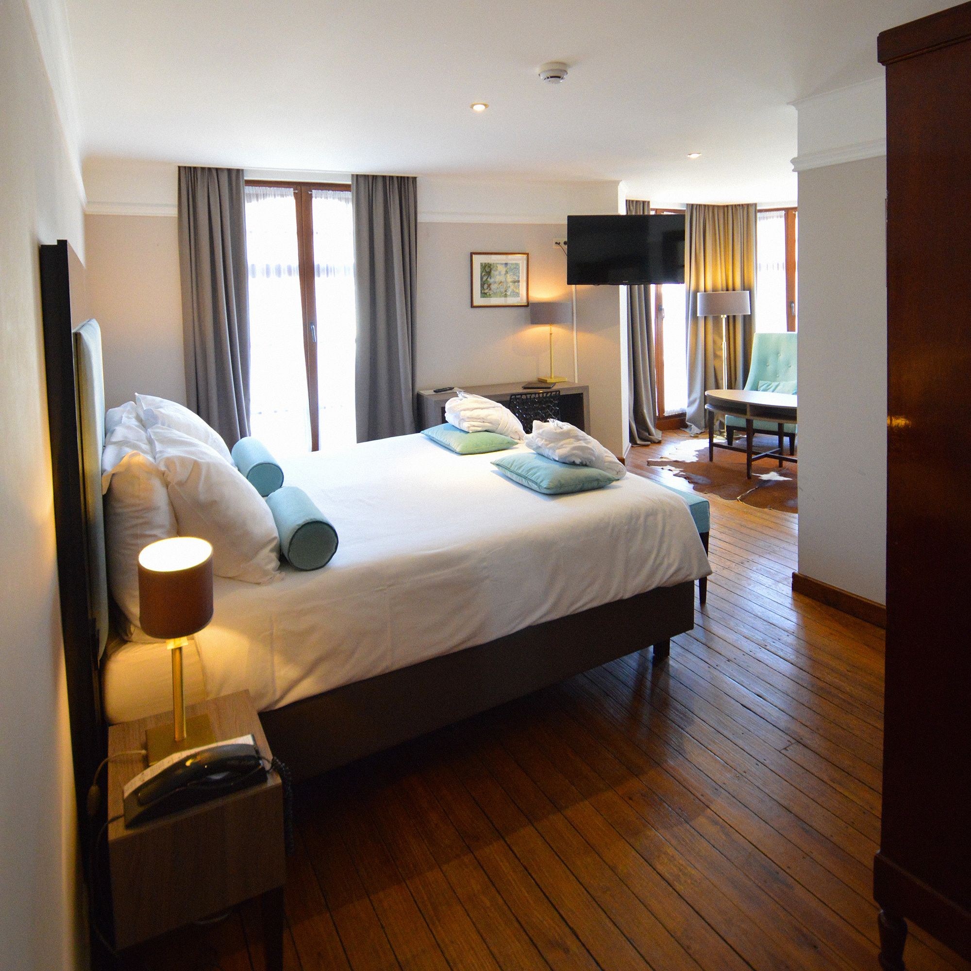 A hotel room with a large bed, a desk with a lamp, a chair, and a television.