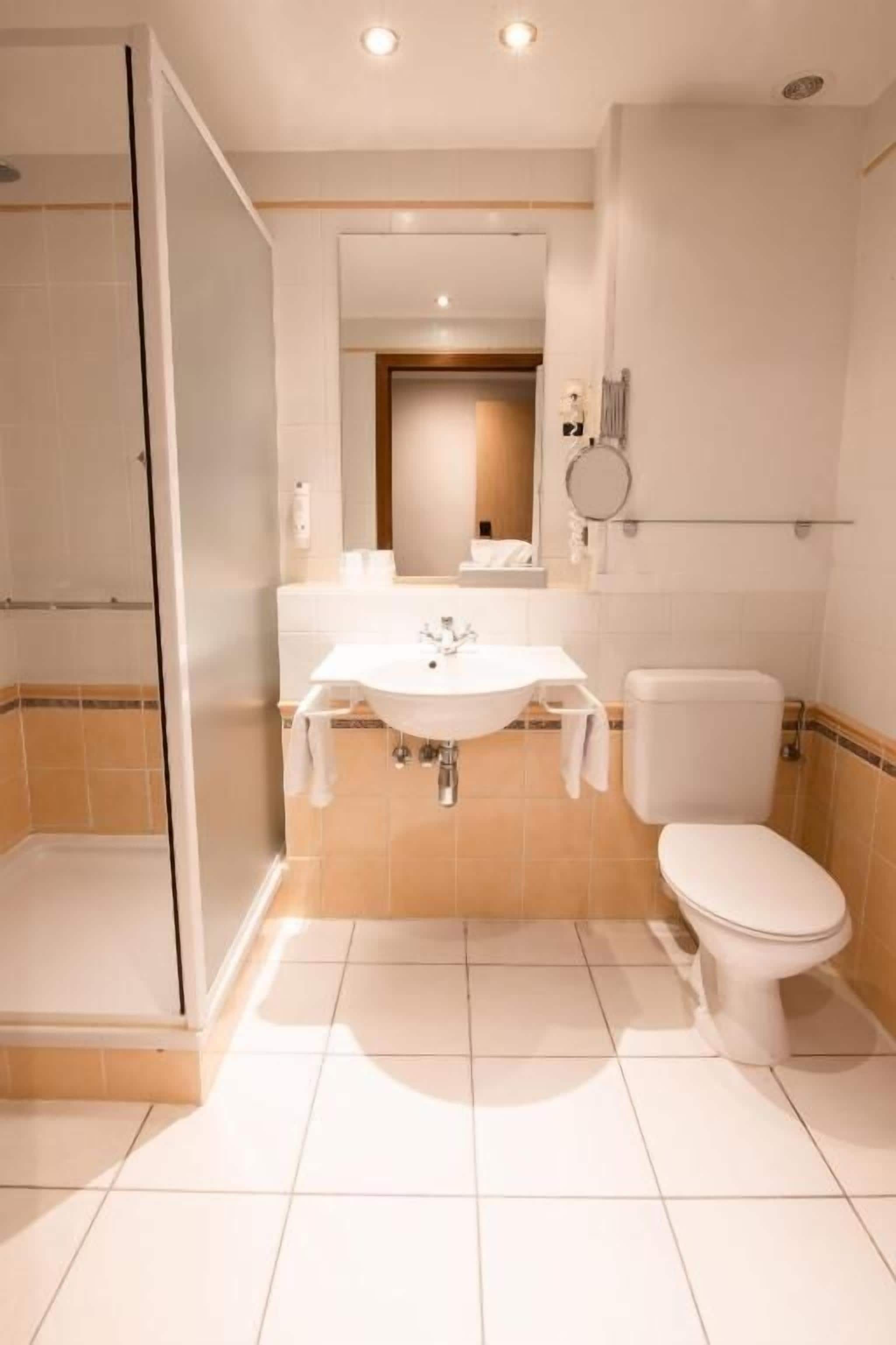 Un baño con ducha, lavamanos, inodoro y espejo.