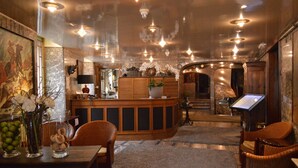 A spacious lobby with a wooden reception desk, comfortable seating, and a large painting on the wall. - Hotel de la Poste - Relais Napoléon III (Bouillon)