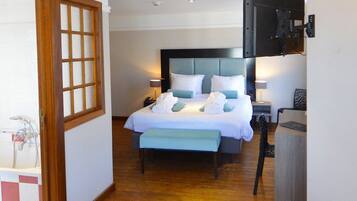 Habitación de hotel con una cama grande, mesitas de noche, una mesa redonda y vistas al exterior.