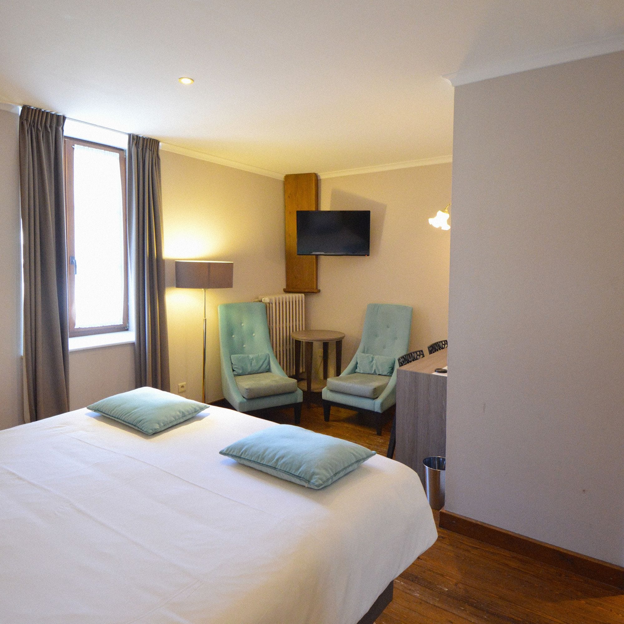 Habitación de hotel con una cama grande, dos sillones, una mesita, un televisor montado en la pared y un radiador.
