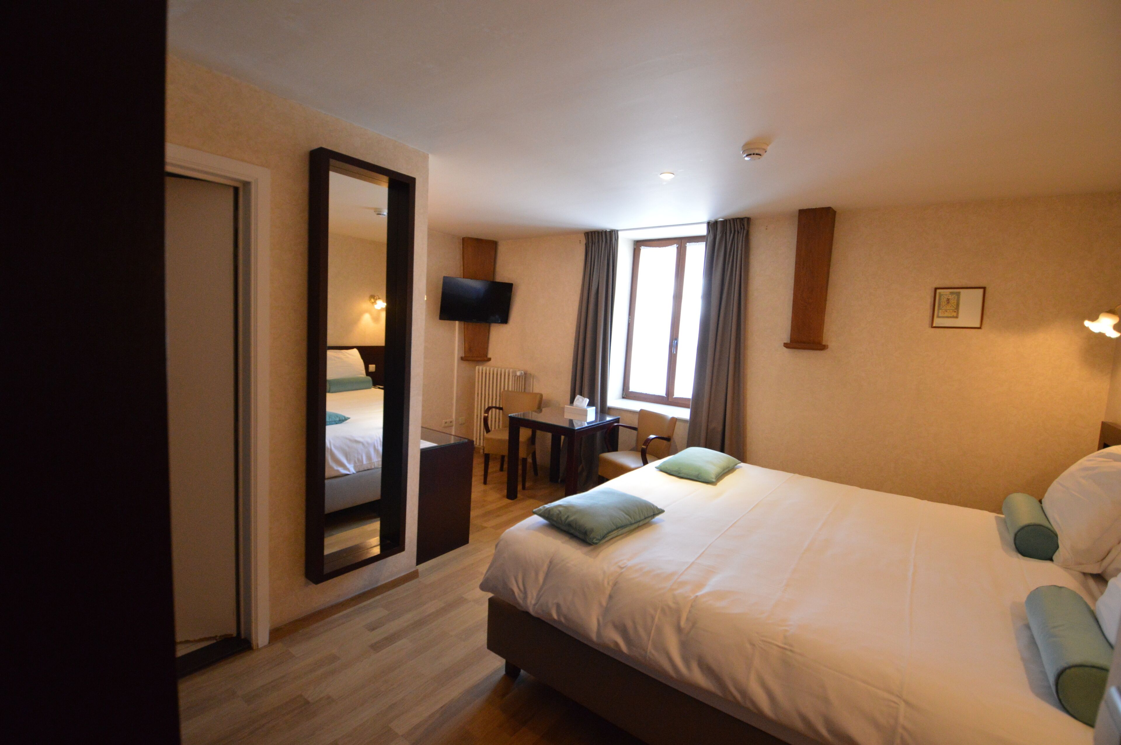 Una habitación de hotel con una cama grande, un escritorio, una silla, un televisor y una ventana con cortinas.