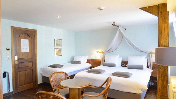 A hotel room with a large bed, two smaller beds, a dining table, wicker chairs, and a canopy bed. - Hotel de la Poste - Relais Napoléon III (Bouillon)