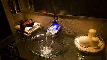 Ein Badezimmer mit einem Glaswaschbecken, einem blauen Wasserhahn und einer Schale Kerzen.