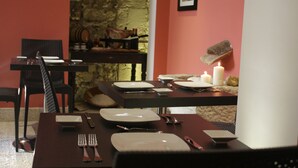 Un comedor con pared de piedra, una mesa preparada para cuatro personas con platos, cubiertos y velas.