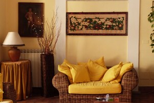 Una sala de estar con un sofá de mimbre, una mesa con lámpara y un cuadro en la pared.