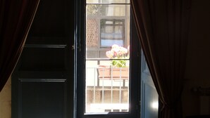 Une pièce dotée d’une grande fenêtre, de rideaux et offrant une vue sur un balcon avec une balustrade et des plantes en pot.