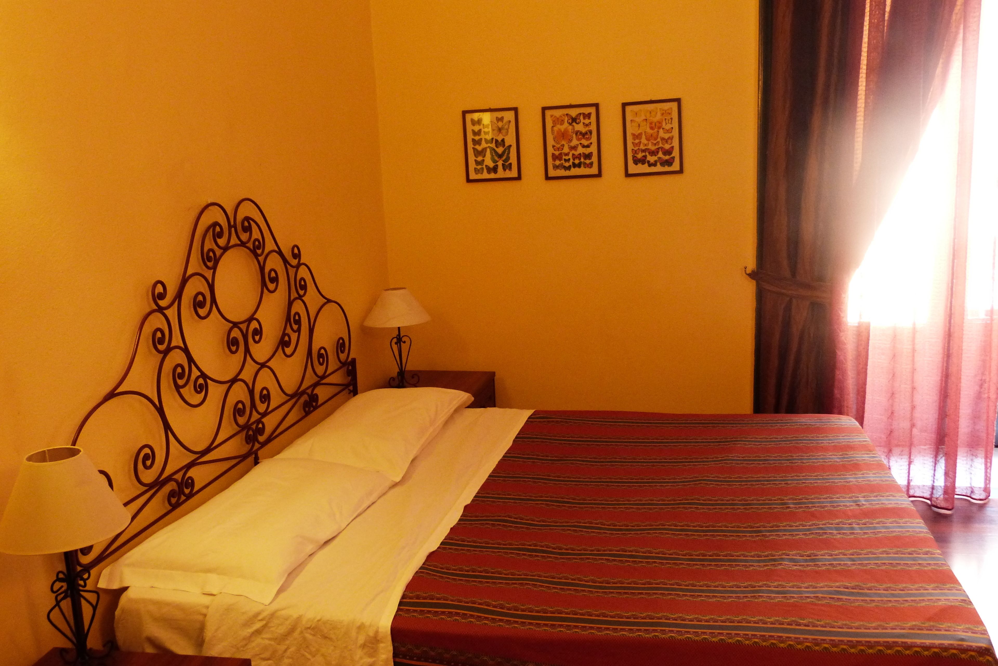 A bed with a metal headboard, a bedside lamp, and a red-striped bedspread. There are three framed pictures on the wall.