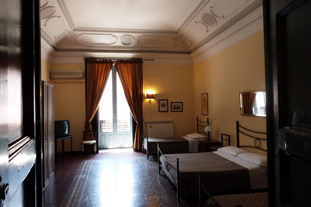 Une chambre d’hôtel avec deux lits, une télévision, un radiateur et une vue sur l’extérieur par une porte.