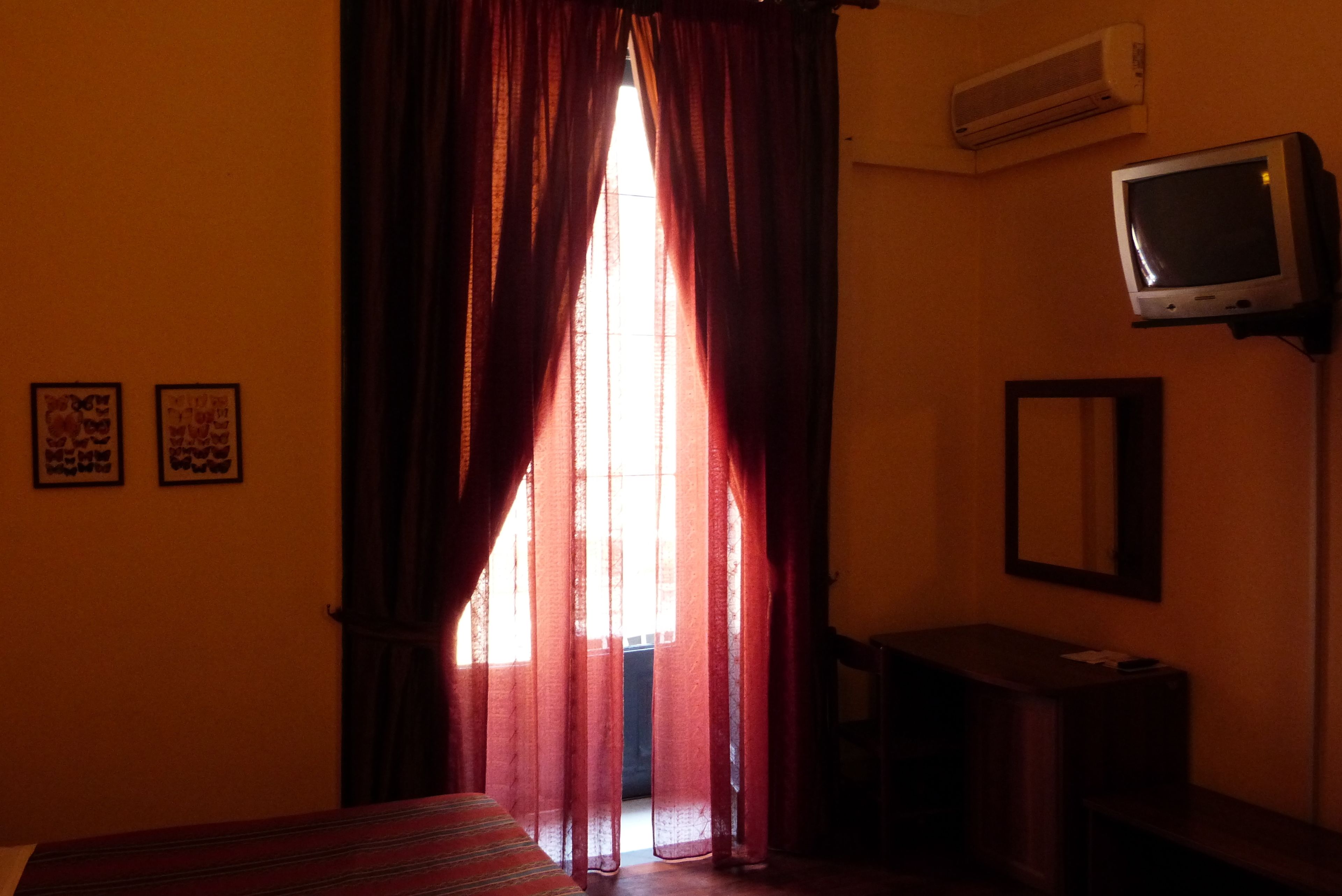 A room with a bed, a desk, a television, and a window with curtains.