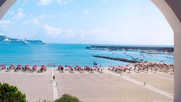 A beach with umbrellas and people, a clear sky, and boats in the water. - Sporting Baia Hotel (Giardini Naxos)