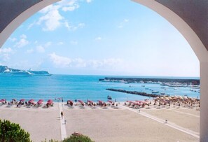 A beach with umbrellas and people, a clear sky, and boats in the water. - Sporting Baia Hotel (Giardini Naxos)