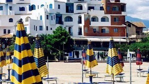 A coastal area with white buildings, beach umbrellas, and lounge chairs. - Sporting Baia Hotel (Giardini Naxos)