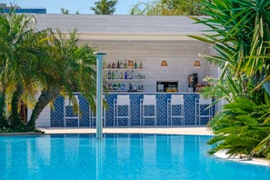 Zona de piscina amb bar, parets de rajola blava i palmeres.
