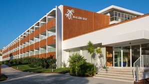 Un moderno edificio de hotel con un logotipo destacado, múltiples balcones y un jardín bien cuidado.