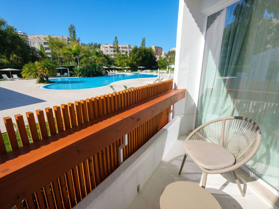 A balcony with a wooden railing overlooking a swimming pool area with lounge chairs and umbrellas.